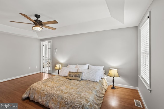 bedroom with wood finished floors, a raised ceiling, visible vents, and baseboards