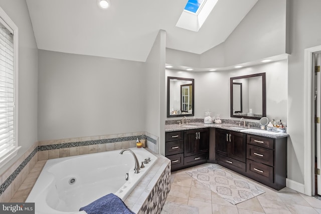 bathroom featuring double vanity, lofted ceiling with skylight, a jetted tub, and a sink