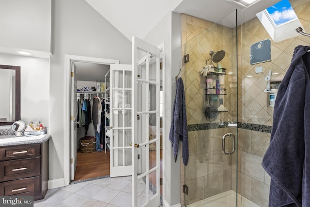 bathroom with vaulted ceiling with skylight, a stall shower, tile patterned floors, french doors, and vanity