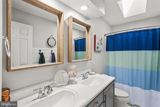 bathroom featuring double vanity, a skylight, toilet, and a sink