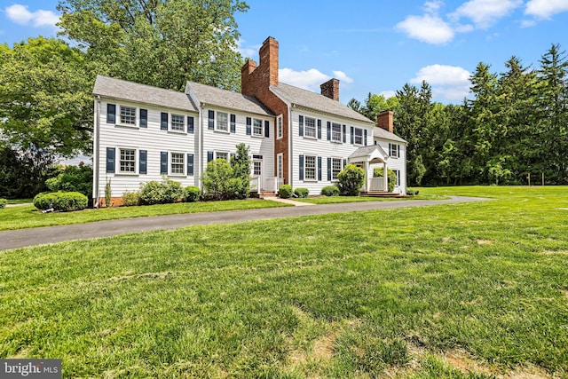 colonial home featuring a front lawn, a chimney, and driveway