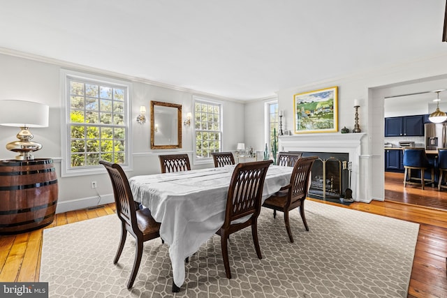 dining area featuring ornamental molding, light wood finished floors, a fireplace with flush hearth, and baseboards