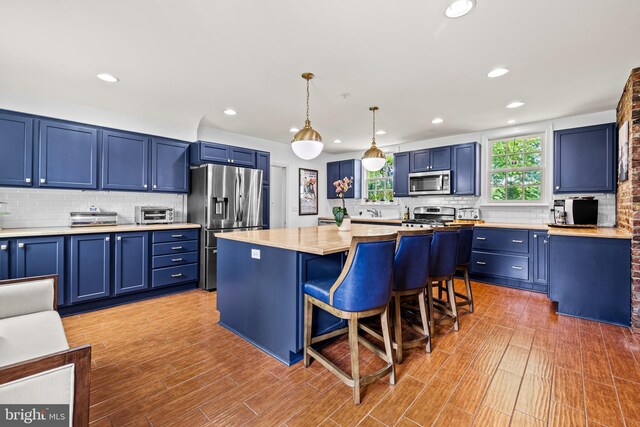 kitchen with stainless steel appliances, blue cabinetry, decorative backsplash, a breakfast bar, and recessed lighting