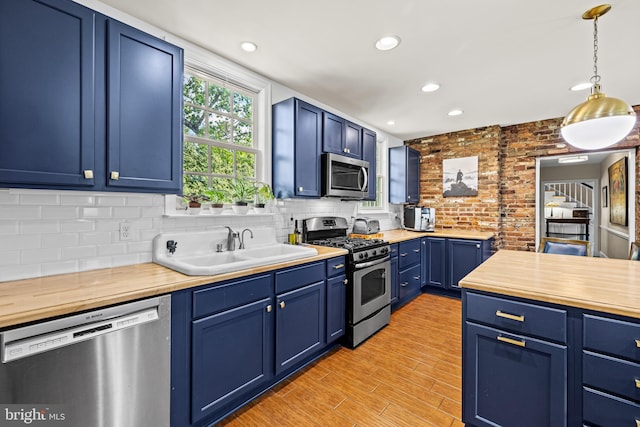 kitchen with appliances with stainless steel finishes, blue cabinetry, butcher block counters, a sink, and recessed lighting