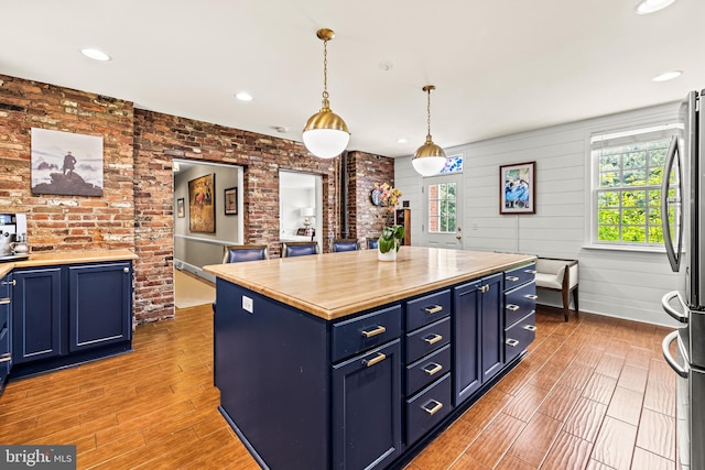 kitchen featuring blue cabinets, freestanding refrigerator, wood finished floors, hanging light fixtures, and brick wall