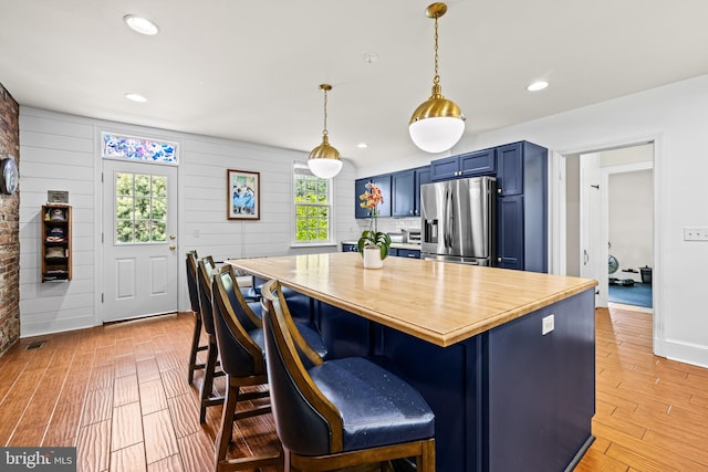 kitchen featuring stainless steel refrigerator with ice dispenser, blue cabinets, plenty of natural light, light wood-type flooring, and recessed lighting