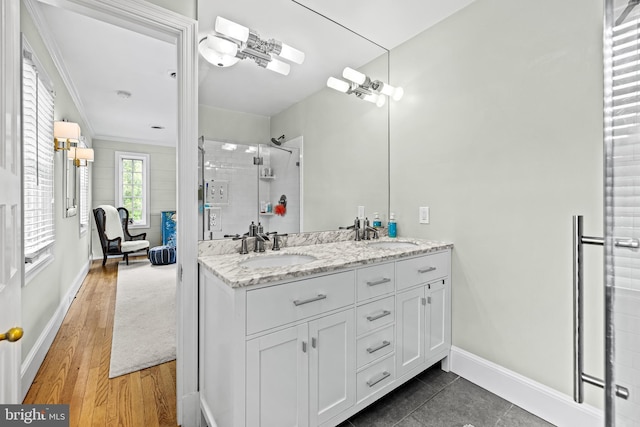bathroom with a shower stall, double vanity, baseboards, wood finished floors, and ornamental molding