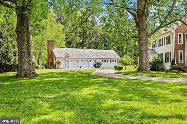 view of front of property featuring driveway, an attached garage, a chimney, and a front lawn