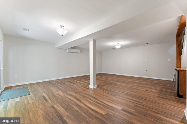 finished basement with a wall mounted AC, dark wood finished floors, and baseboards