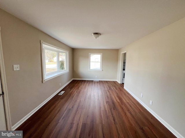 spare room with baseboards, visible vents, and dark wood finished floors