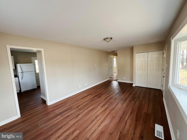unfurnished bedroom featuring dark wood-type flooring, freestanding refrigerator, visible vents, and baseboards