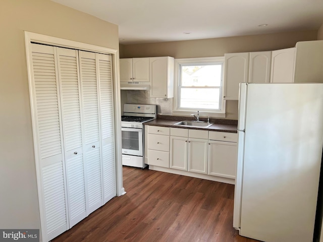 kitchen featuring white cabinets, a sink, dark countertops, white appliances, and under cabinet range hood