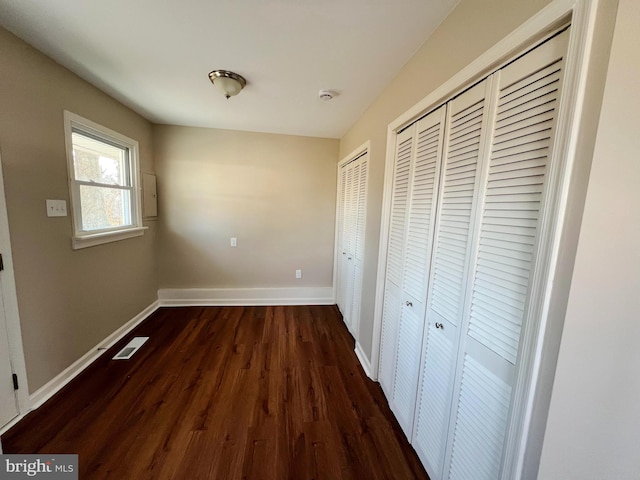 interior space featuring baseboards, visible vents, two closets, and dark wood-style flooring