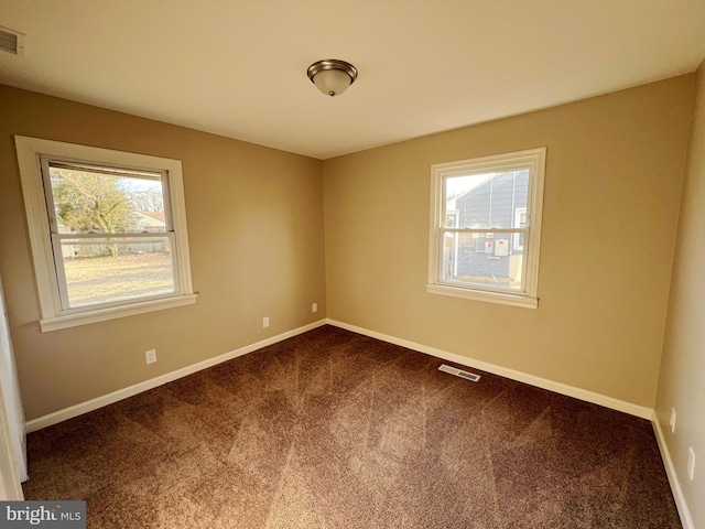 empty room featuring dark carpet, visible vents, and baseboards