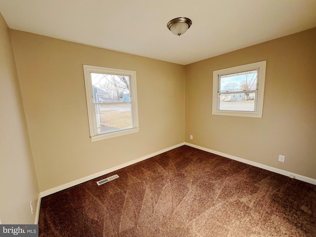 spare room with dark colored carpet, visible vents, and baseboards