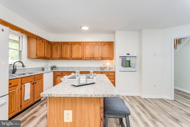 275 Wood Rise Ln, Winchester, VA 22602 - kitchen featuring a breakfast bar area, a sink, light stone counters, light wood-style floors, and white appliances