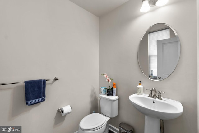 half bath featuring baseboards, a sink, and toilet