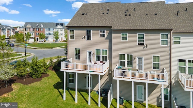 rear view of property featuring a residential view, a shingled roof, a deck, cooling unit, and a lawn