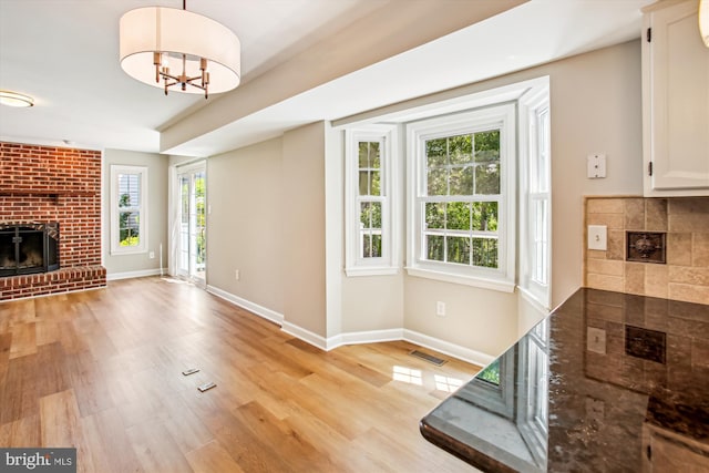 21130 Haystack Ct, Ashburn, VA 20147 - unfurnished living room featuring a brick fireplace, baseboards, light wood-style floors, and a chandelier
