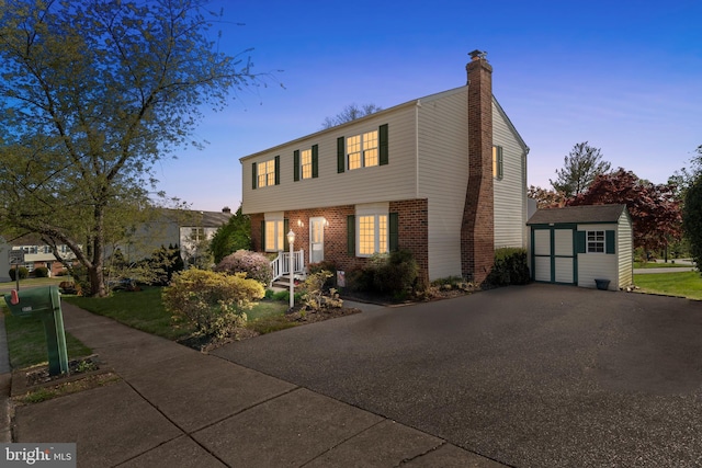 colonial inspired home with a storage unit, a chimney, brick siding, and an outdoor structure