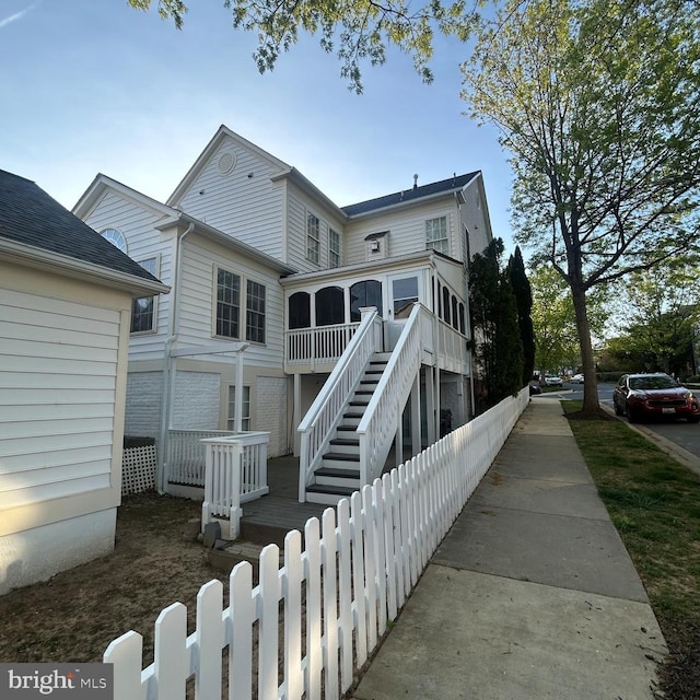 rear view of property with fence, stairs, and a sunroom