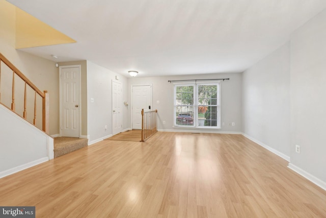 unfurnished living room featuring stairs, baseboards, and light wood-style floors