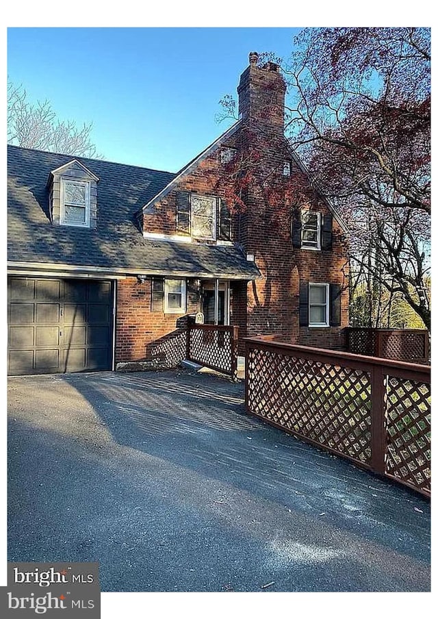 view of front of home with brick siding, a chimney, a garage, and aphalt driveway