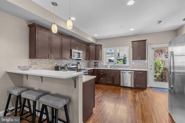 kitchen featuring dark wood-style flooring, stainless steel appliances, visible vents, backsplash, and a peninsula
