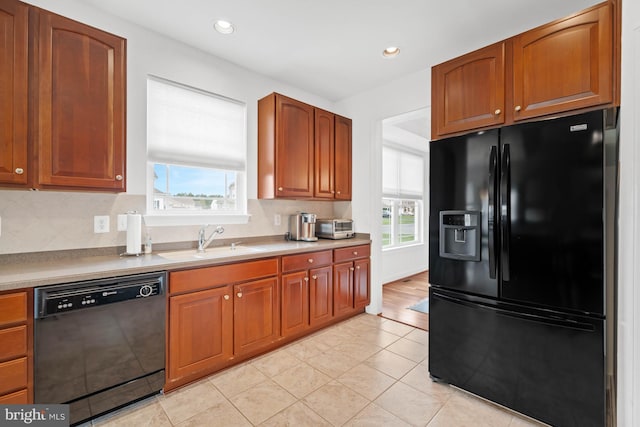 kitchen featuring light tile patterned floors, a sink, black appliances, and a healthy amount of sunlight