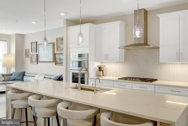 kitchen with wall chimney exhaust hood, appliances with stainless steel finishes, open floor plan, decorative backsplash, and a kitchen bar