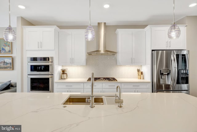 kitchen featuring stainless steel appliances, wall chimney exhaust hood, white cabinetry, backsplash, and recessed lighting