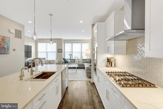 kitchen featuring wall chimney exhaust hood, a sink, stainless steel appliances, open floor plan, and white cabinets