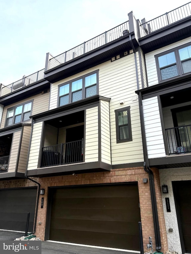rear view of property featuring a balcony, a garage, and brick siding