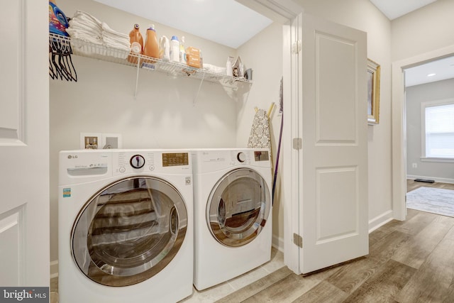 clothes washing area with wood finished floors, separate washer and dryer, and baseboards