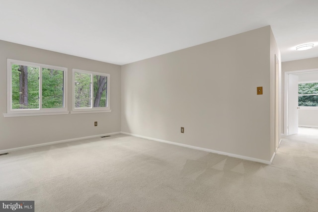 spare room with baseboards, visible vents, and light carpet