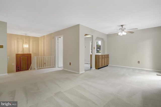 unfurnished living room featuring baseboards, light carpet, and ceiling fan with notable chandelier