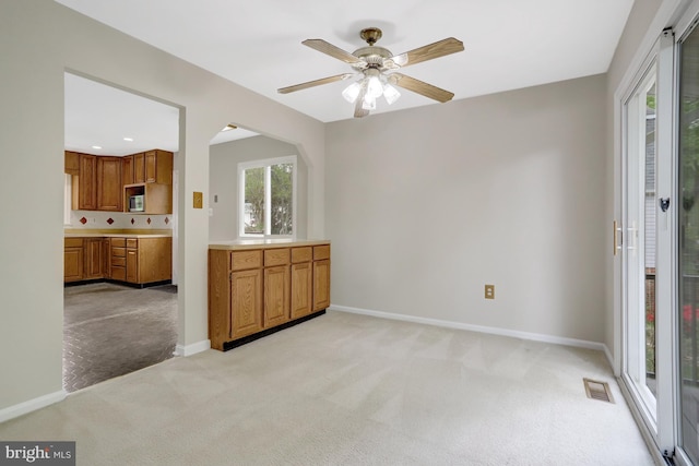 interior space featuring baseboards, light colored carpet, ceiling fan, and visible vents