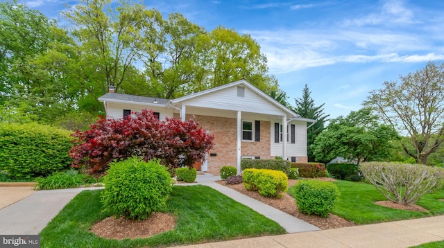 neoclassical home featuring brick siding, a front lawn, covered porch, and a chimney