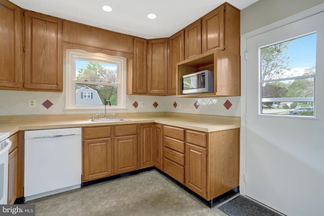 kitchen featuring white dishwasher, a sink, stainless steel microwave, and backsplash
