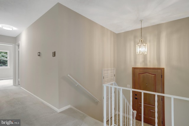 hallway with an inviting chandelier, baseboards, carpet, and an upstairs landing