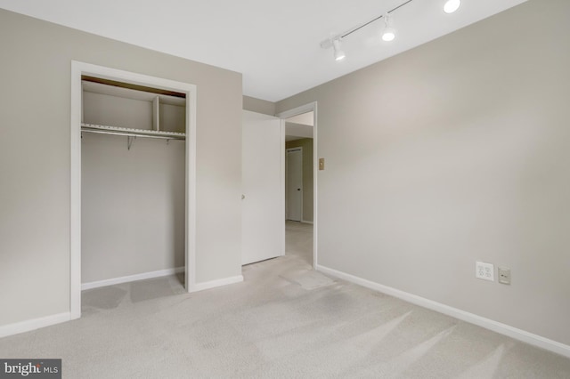 unfurnished bedroom featuring baseboards, carpet flooring, rail lighting, and a closet