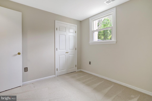 unfurnished bedroom with baseboards, light colored carpet, visible vents, and a closet