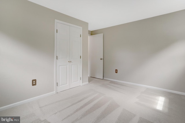 unfurnished bedroom featuring baseboards, a closet, and light colored carpet