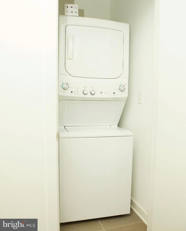 washroom with baseboards, stacked washer and clothes dryer, tile patterned flooring, and laundry area