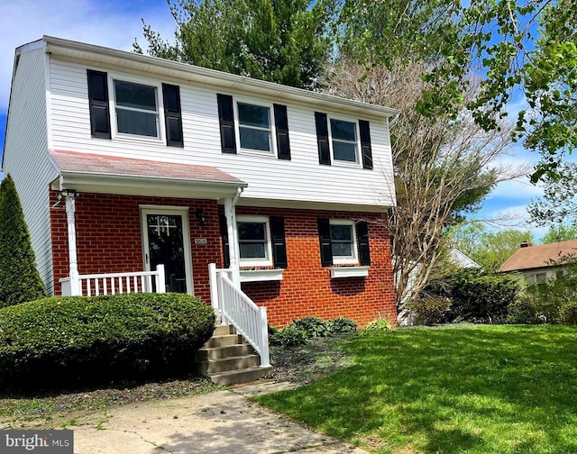 view of front of home with brick siding, a front lawn, and covered porch