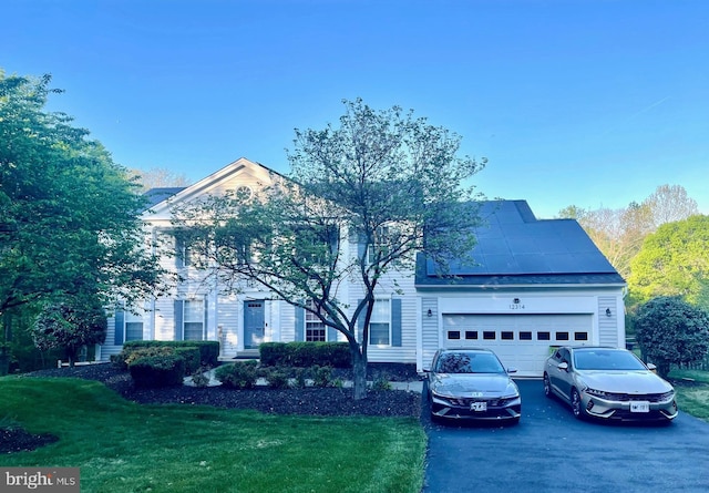 view of front of property featuring an attached garage, a front yard, solar panels, and aphalt driveway