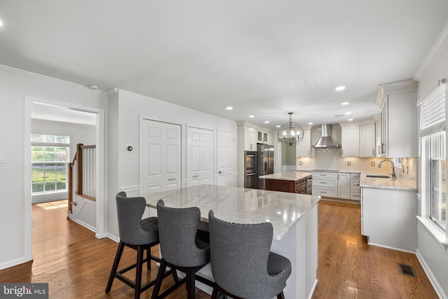 kitchen featuring wall chimney range hood, a sink, tasteful backsplash, a kitchen island, and visible vents