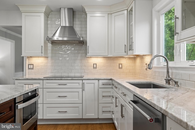 kitchen featuring a sink, appliances with stainless steel finishes, white cabinets, and wall chimney range hood