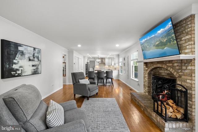 living area featuring a brick fireplace, recessed lighting, baseboards, wood finished floors, and ornamental molding