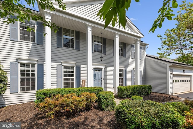 neoclassical / greek revival house featuring a porch, an attached garage, and driveway